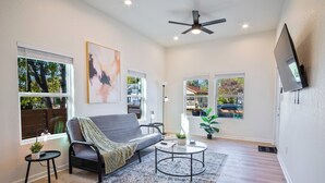 A living room with a grey sofa, a round coffee table, and a flat-screen TV mounted on the wall.