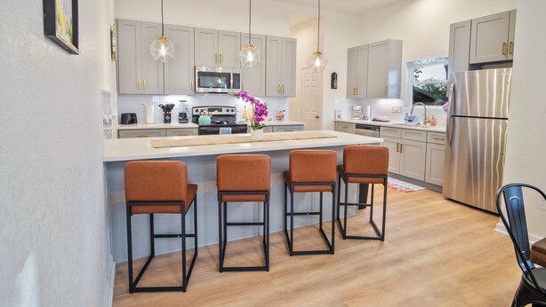 A modern kitchen with grey cabinets, a stainless steel refrigerator, and a central island with bar stools.