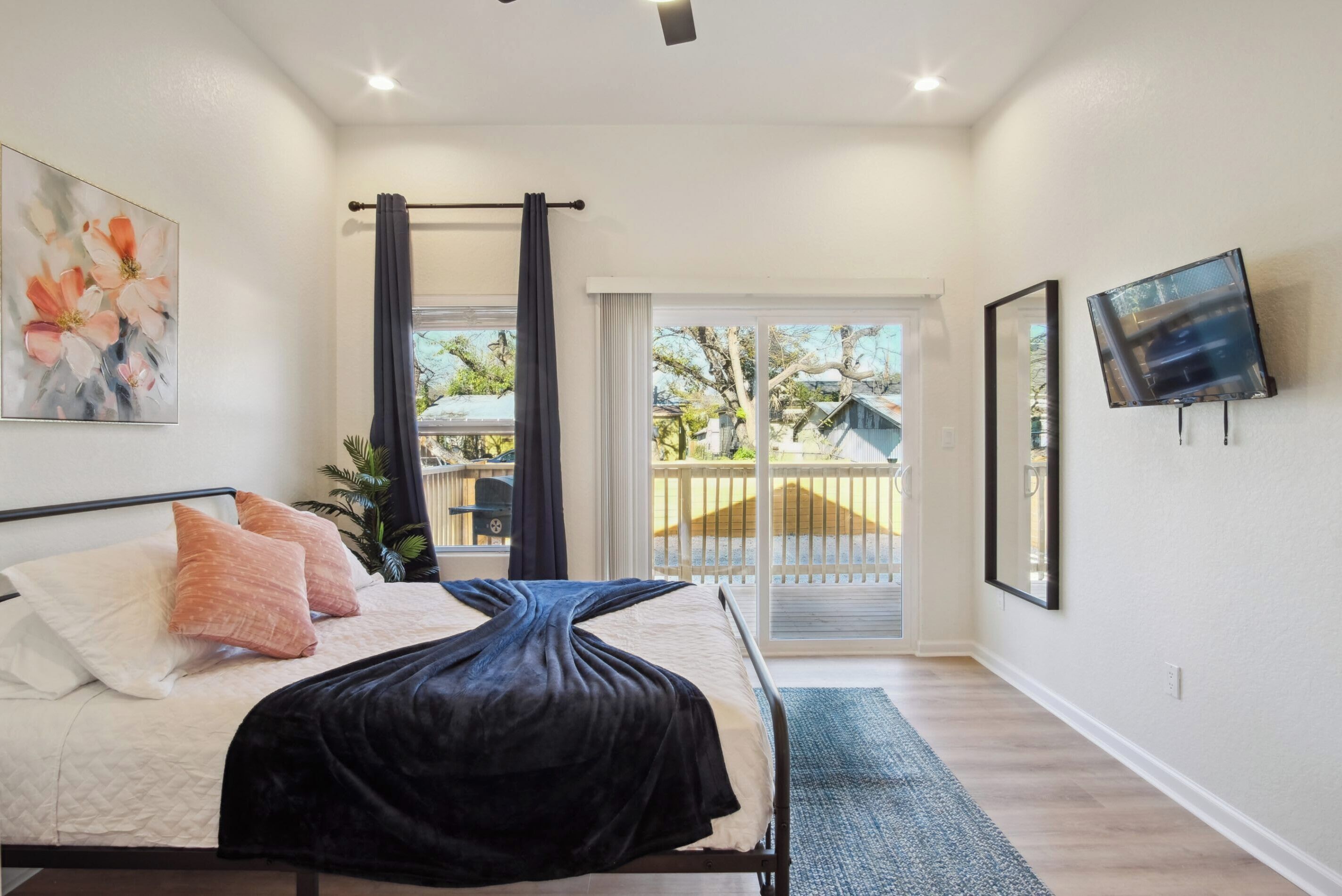 A bedroom with a bed, a TV, a painting, and a view of the outside.