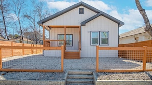 A two-story house with a front porch, wooden fence, and gravel driveway. - Feel, Chill and Enjoy 4BR/3BA Near Fun Riverwalk! (San Antonio)