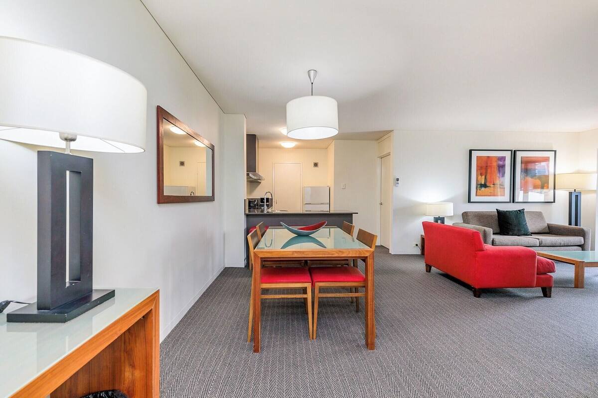 A modern hotel room with a dining area, a sofa, and a kitchen in the background.