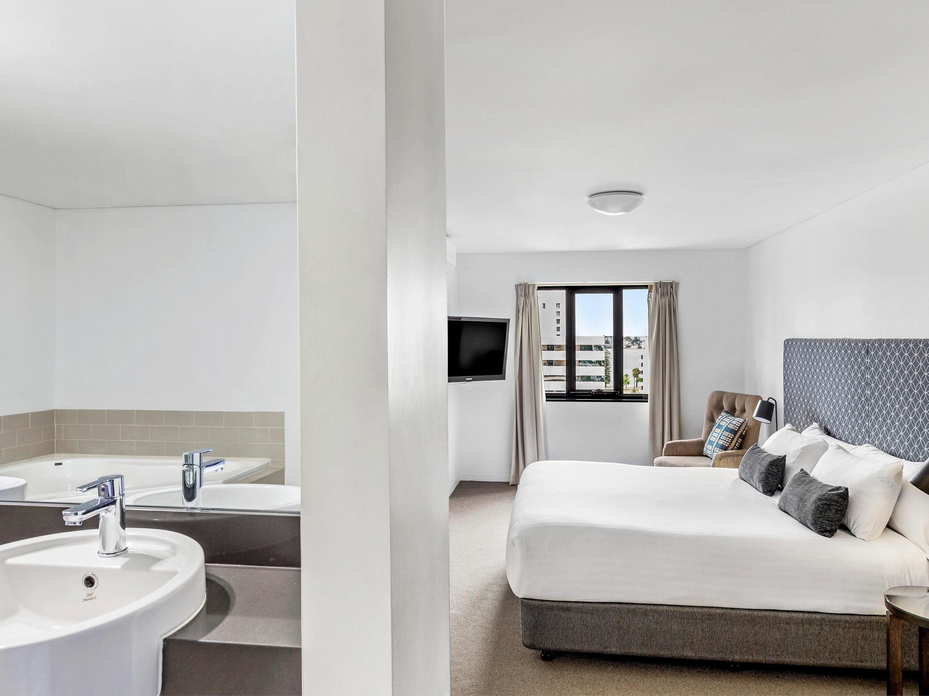 Une chambre d’hôtel équipée d’un lit, d’une télévision, d’une fenêtre et d’une salle de bain avec un lavabo et un miroir.