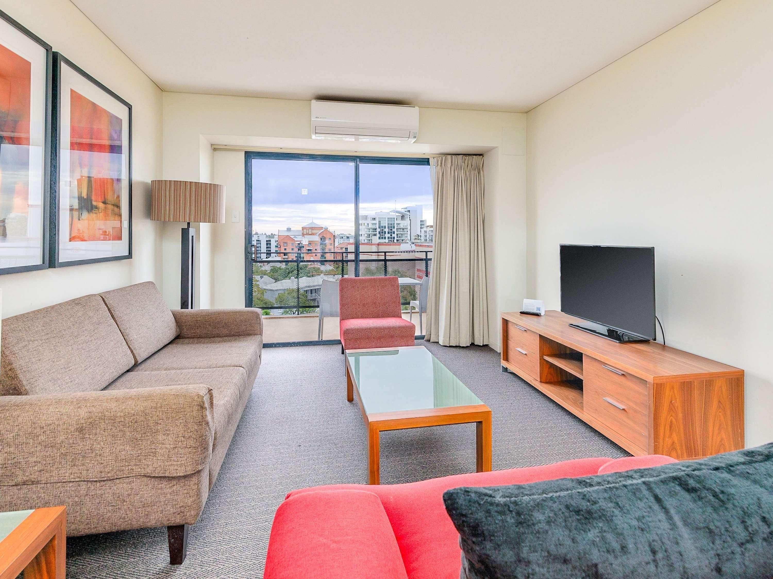 Habitación de hotel con sofá, sillón, televisión y balcón con vistas a la ciudad.
