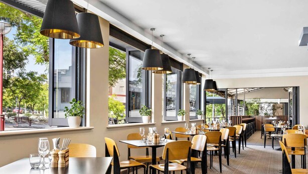A restaurant with tables and chairs, large windows, and hanging pendant lights.