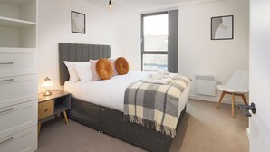 A bedroom with a bed, bedside table, lamp, and a window with a view.