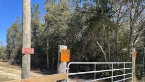 A gated entrance with a wooden fence and metal gate, a red sign with the number 5968, and a posted sign indicating private property with hunting and fishing restrictions. - Country Cabin in Private Setting (Altha)