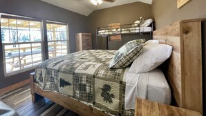 A bedroom with a large bed, a ceiling fan, a window with blinds, and a bunk bed in the background. - Country Cabin in Private Setting (Altha)