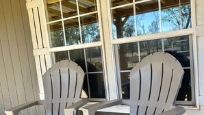 Two Adirondack chairs on a wooden deck with a view of a house through large windows. - Country Cabin in Private Setting (Altha)