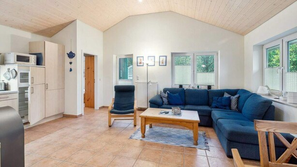A spacious living area with a high ceiling, a blue sofa set, a wooden coffee table, and a kitchen area with a microwave and cabinets. - 4 Star Holiday Home in Ottendorf (Otterndorf)