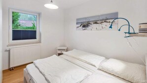 A bedroom with a bed, a window with blinds, a radiator, a bedside table, and wall art. - 4 Star Holiday Home in Ottendorf (Otterndorf)