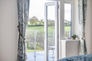 A room with a large window, a bed, and a view of a green landscape. - 3 Bed in Plympton (oc-m30351) (Sparkwell)