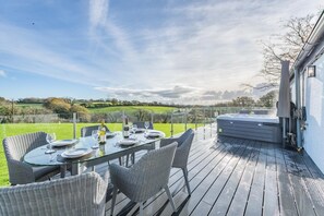 Un área de comedor al aire libre con una mesa preparada para cuatro personas, rodeada de sillas de mimbre y vistas a un paisaje pintoresco.