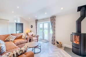 A modern living room with a sofa set, a coffee table, a fireplace, and a view through the glass doors. - 3 Bed in Plympton (oc-m30351) (Sparkwell)