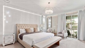 Quarto moderno com cama grande, mesas de cabeceira, um banco, um candelabro e vista para o exterior.