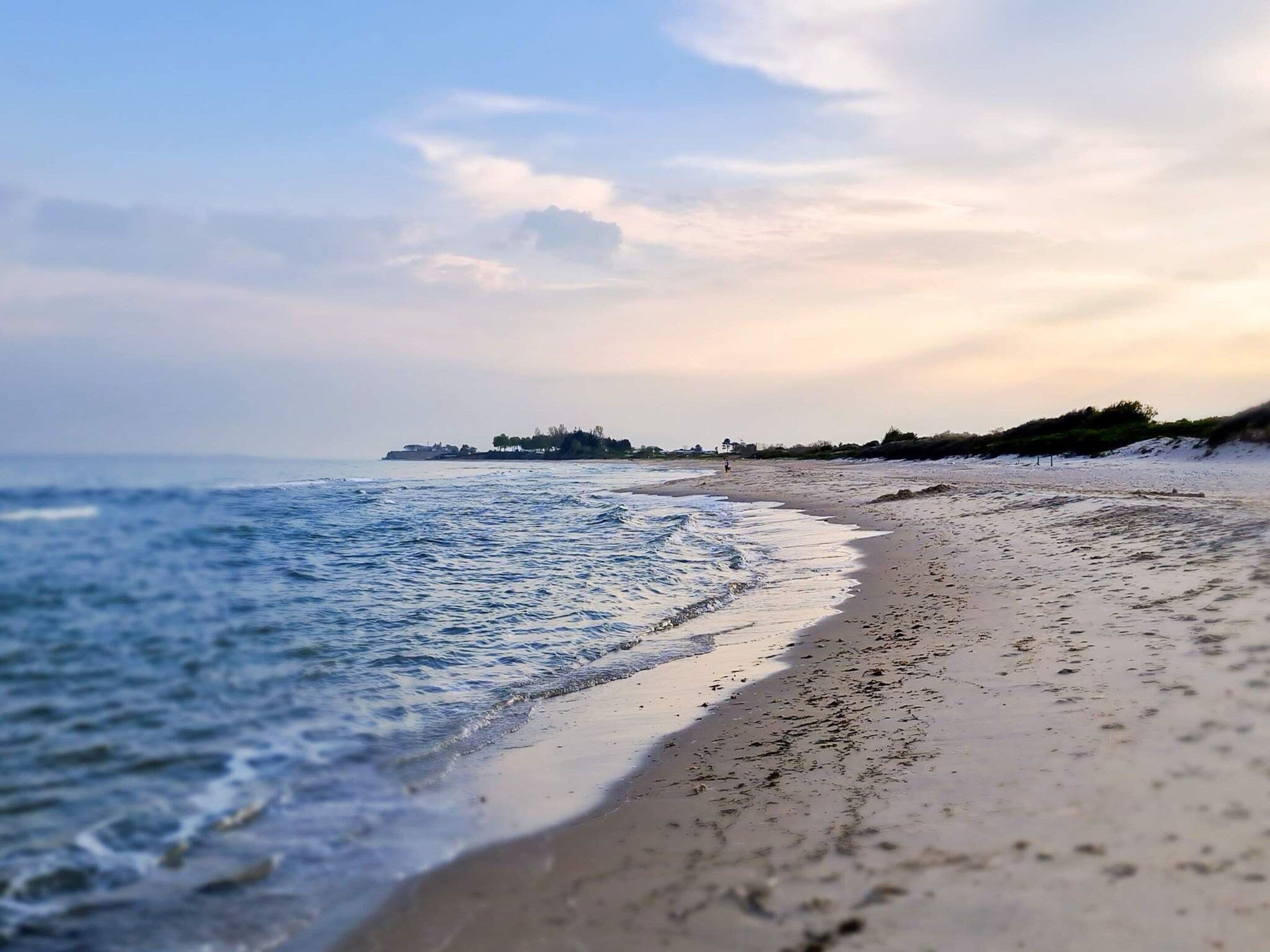 A beach with a calm sea, a sandy shore, and a distant shoreline with buildings.