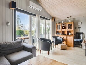 A modern living room with a grey sofa, black armchairs, a wooden coffee table, and a kitchen area with wooden cabinets and a clock on the wall. - 4 Star Holiday Home in Sydals (Sydals)