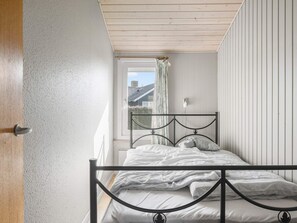 A bedroom with a single bed, a window with curtains, and a wooden ceiling.