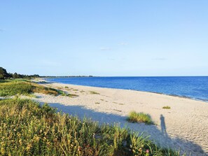 A beach with sand, water, and wind turbines in the distance.