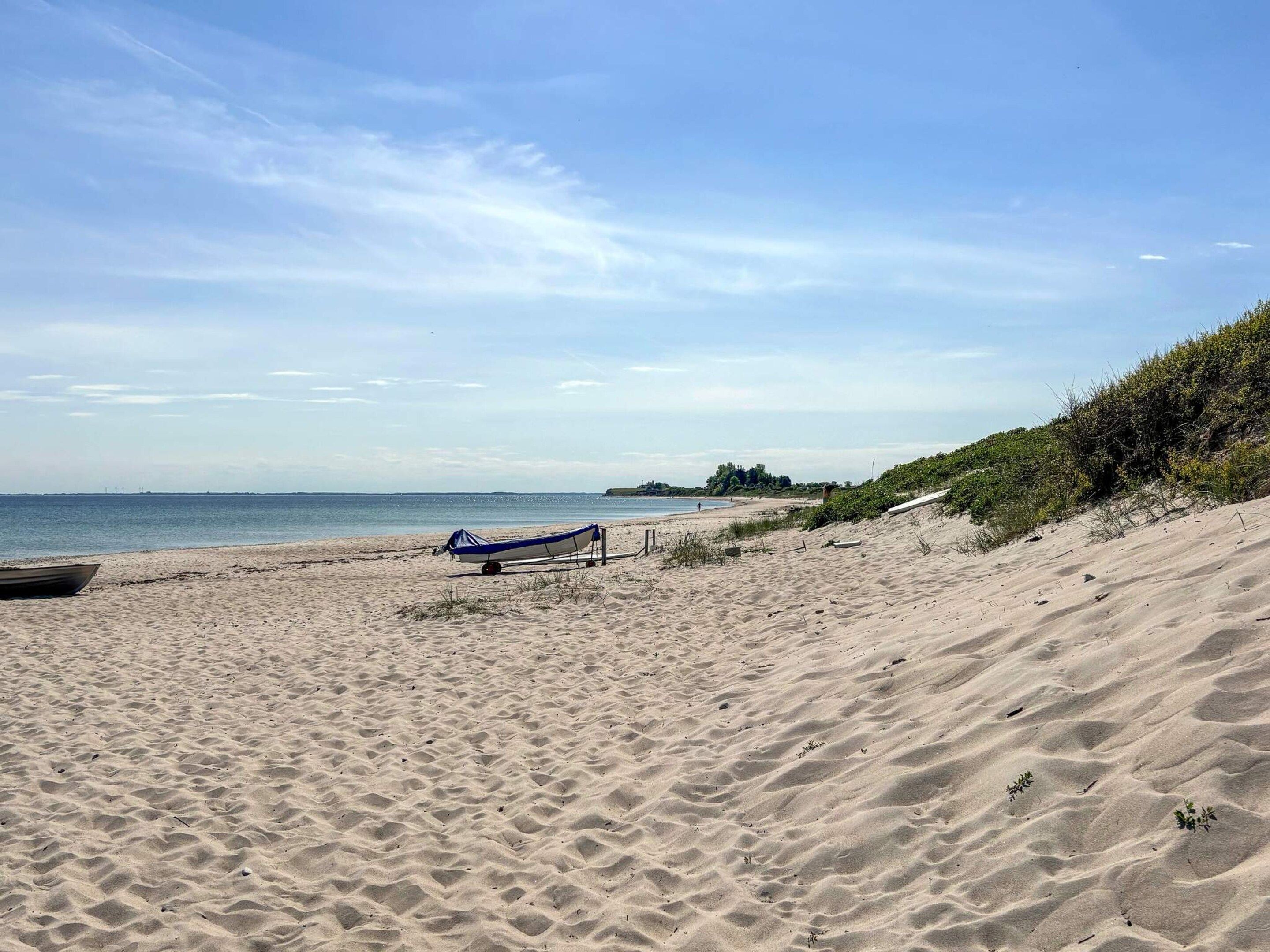 Een zandstrand met een klein bootje en een blauw zonnescherm.