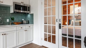 A kitchen with white cabinets, a stainless steel microwave, and a green tiled backsplash. - Plums Unit 2: Downtown - King (Stratford)