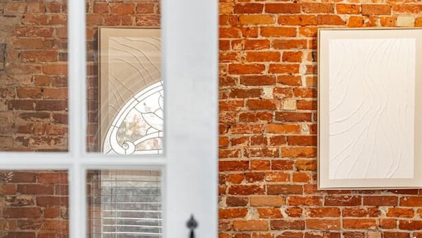 A bedroom with a brick wall, a bed with white linens, and a window with blinds. - Plums Unit 2: Downtown - King (Stratford)