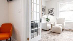 A living room with a white door, a television mounted above it, and a large window with decorative moldings. - Plums Unit 2: Downtown - King (Stratford)