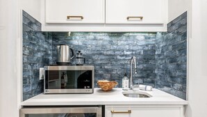 A compact kitchen with white cabinets, a stainless steel microwave, a kettle, and a sink.