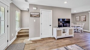 Een ruime woonkamer met houten vloer, een witte tv-meubel, een flatscreen televisie en een eethoek met witte stoelen en een tafel.