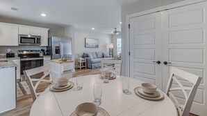 Een moderne keuken met witte kastjes, een magnetron en een koelkast. Er is een eethoek met een ronde tafel en stoelen, en een bank op de achtergrond.