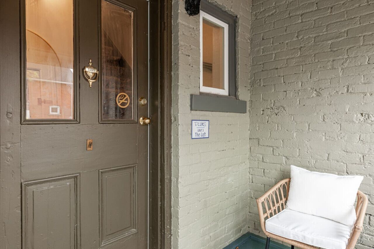 A door with a brass handle and a window, a wicker chair with a cushion, and a sign indicating "Unit 3 The Loft".