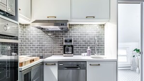 A modern kitchen with white cabinets, a stainless steel dishwasher, and a coffee maker. - Plums Unit 3: Downtown King (Stratford)