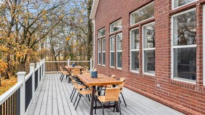 Une terrasse avec une table et des chaises en bois, un bâtiment en briques doté de grandes fenêtres et des arbres aux feuilles d’automne.