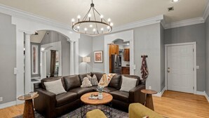 Un salon avec un canapé d’angle en cuir marron, deux tables basses rondes, un fauteuil jaune et un lustre.
