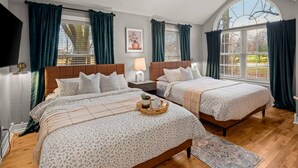 Une chambre avec deux lits, un ventilateur de plafond et de grandes fenêtres avec des rideaux.