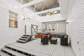 A spacious deck with a hot tub, seating area, and a staircase leading to an upper level. - Arkansas Grand Oasis: Heated Indoor Pool, Hot Tub & More! (Benton County)