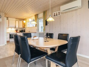 A modern kitchen with wooden cabinets, a dining table with black chairs, and pendant lighting.
