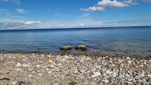 Una playa pedregosa con aguas cristalinas y una costa lejana.
