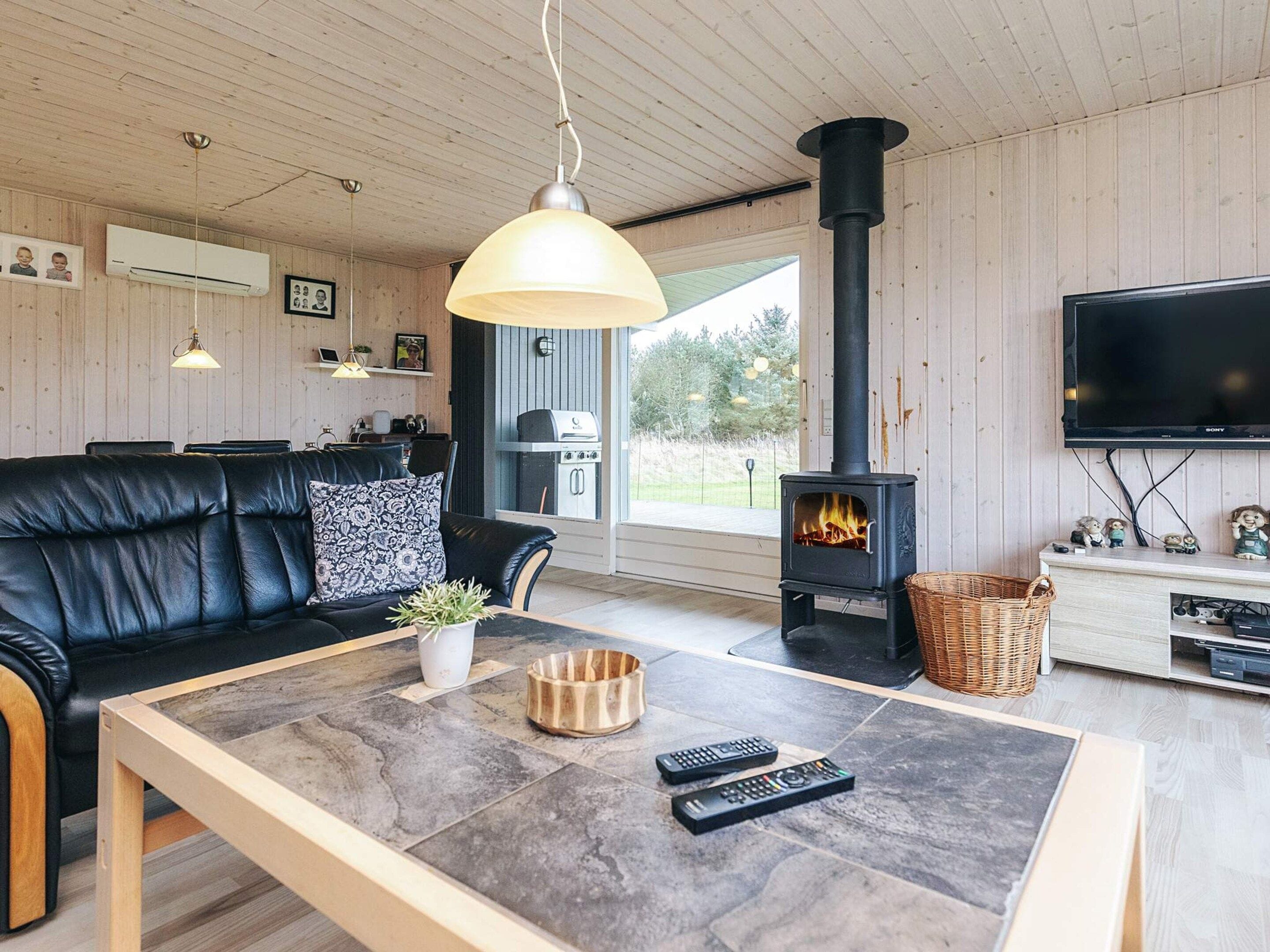 A cozy living room with a black leather sofa, a coffee table with remotes, a fireplace, and a television.