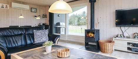 A cozy living room with a black leather sofa, a coffee table with remotes, a fireplace, and a television.