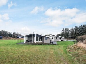 A modern mobile home with a large deck, a covered outdoor area, and a fenced yard.