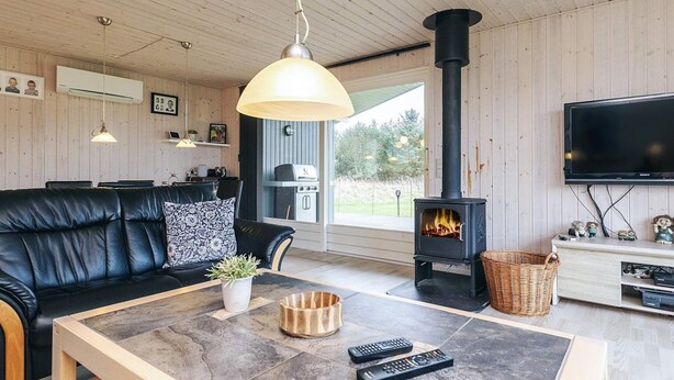 Una sala de estar acogedora con un sofá de cuero negro, una mesita de centro con controles remotos, una chimenea y un televisor montado en la pared.