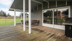 Un patio cubierto con piso de madera, mobiliario exterior y una parrilla.
