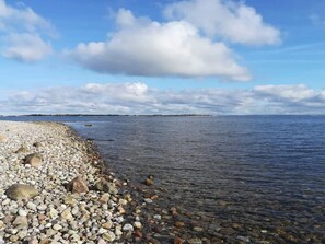 A pebbled beach with clear water and a distant shoreline.