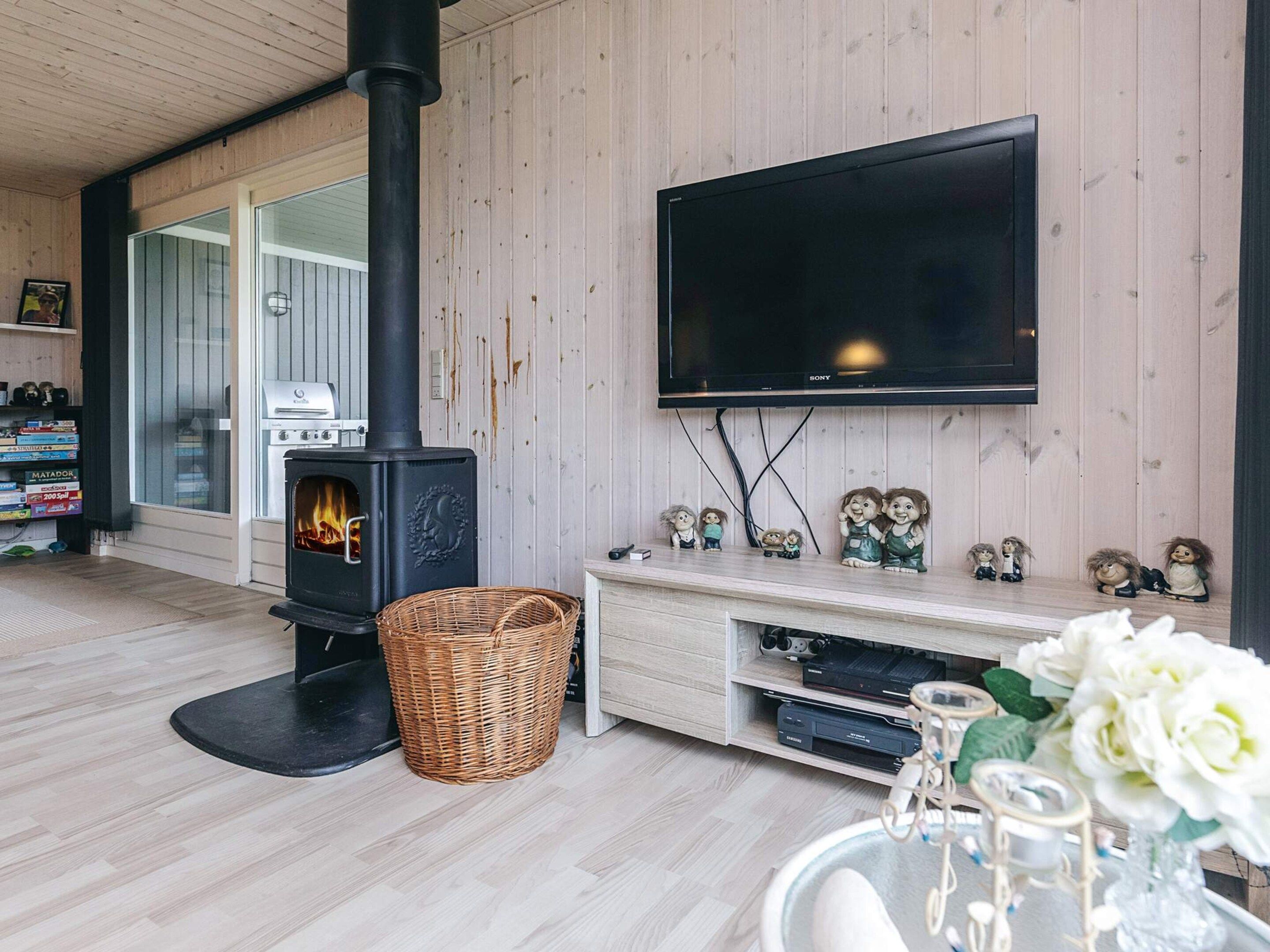 A living room with a wood-burning stove, a flat-screen TV, and a shelf with decorative items.