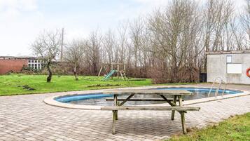 Ein Schwimmbecken mit Holzterrasse, einer Rutsche und einer Schaukel in einer Parkanlage.