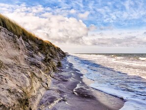 A coastal landscape with a rocky cliff, waves, and a partly cloudy sky. - 2 Person Holiday Home in Hojer (Højer)