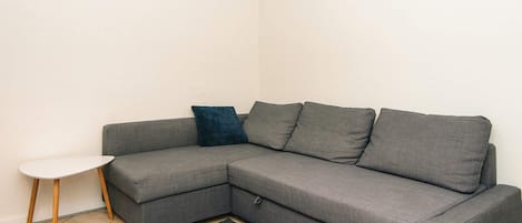 A corner living room with a grey sectional sofa, a small white side table, and a dark grey rug.