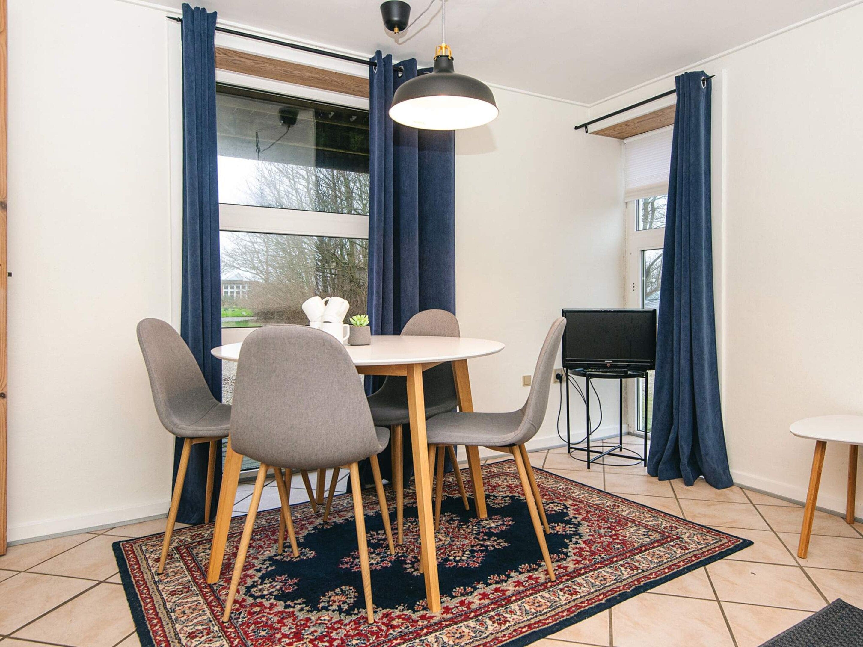 A dining area with a round table, four chairs, a small potted plant, and a television on a stand.