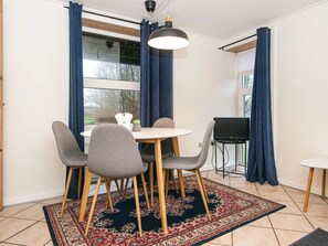 A dining area with a round table, four chairs, a small potted plant, and a television on a stand.