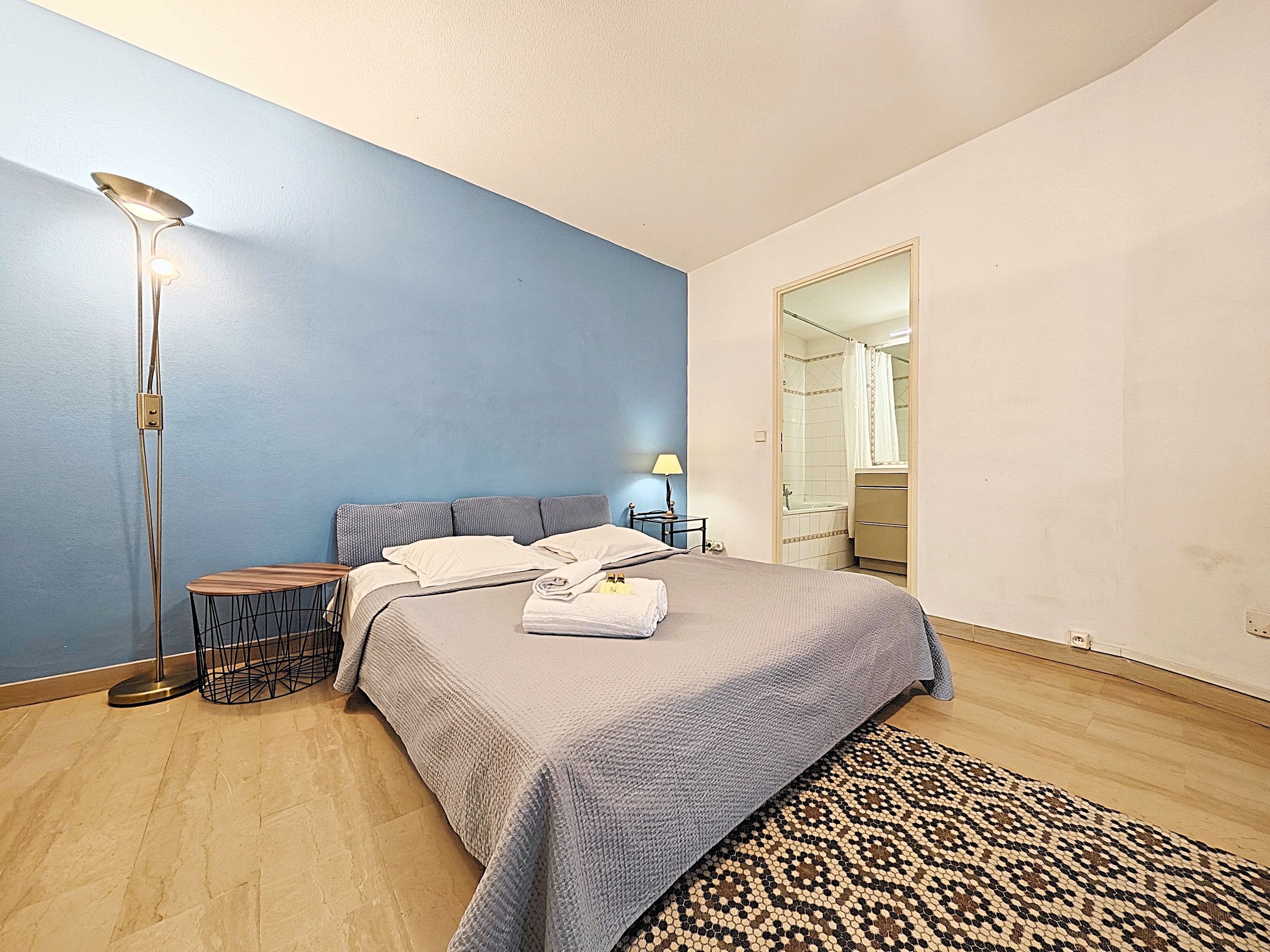 A bedroom with a bed, bedside table, lamp, and a view into the bathroom.
